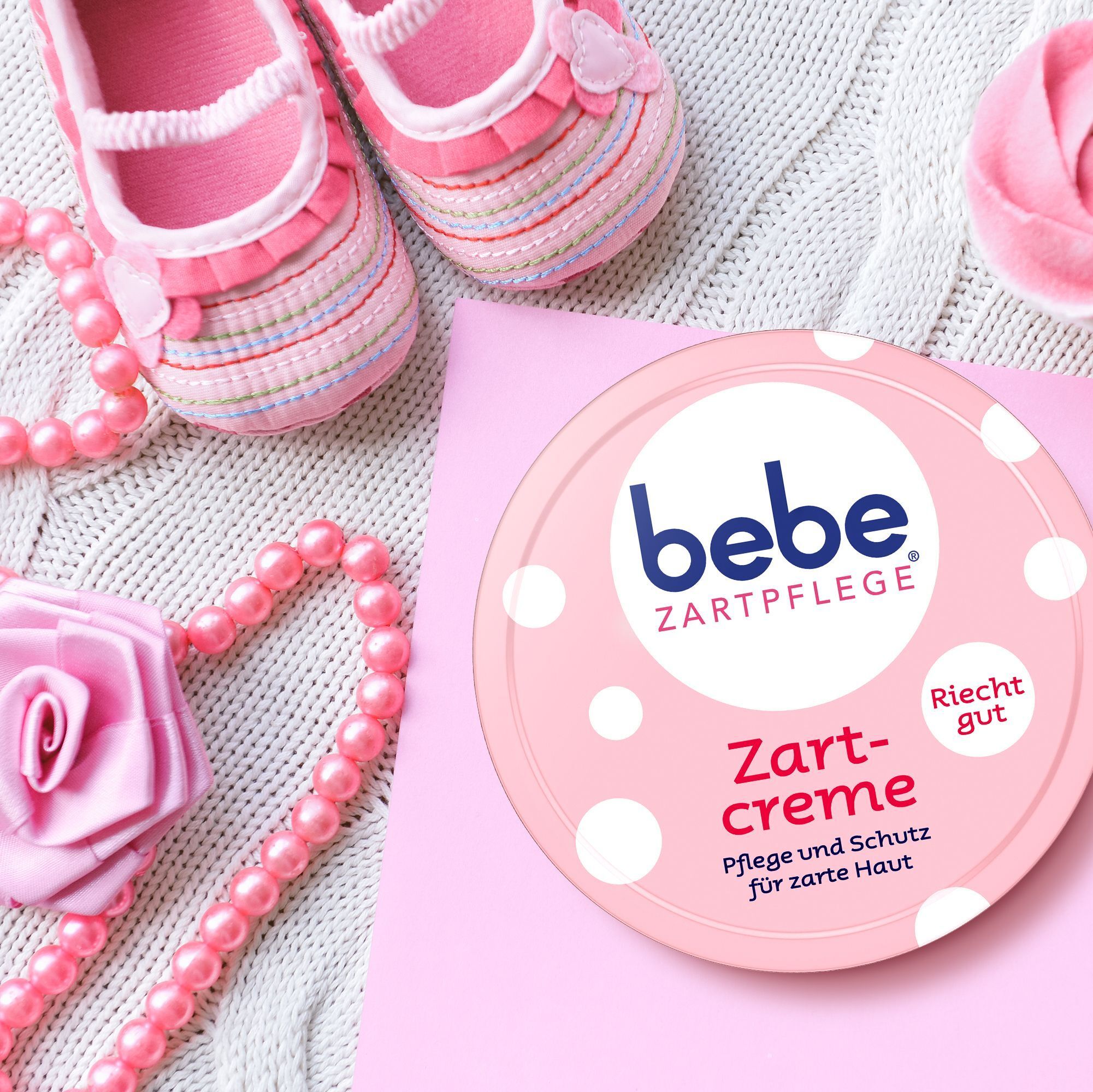 Ein runder Becher 'bebe Zartcreme' neben Babyschuhen und Perlen.