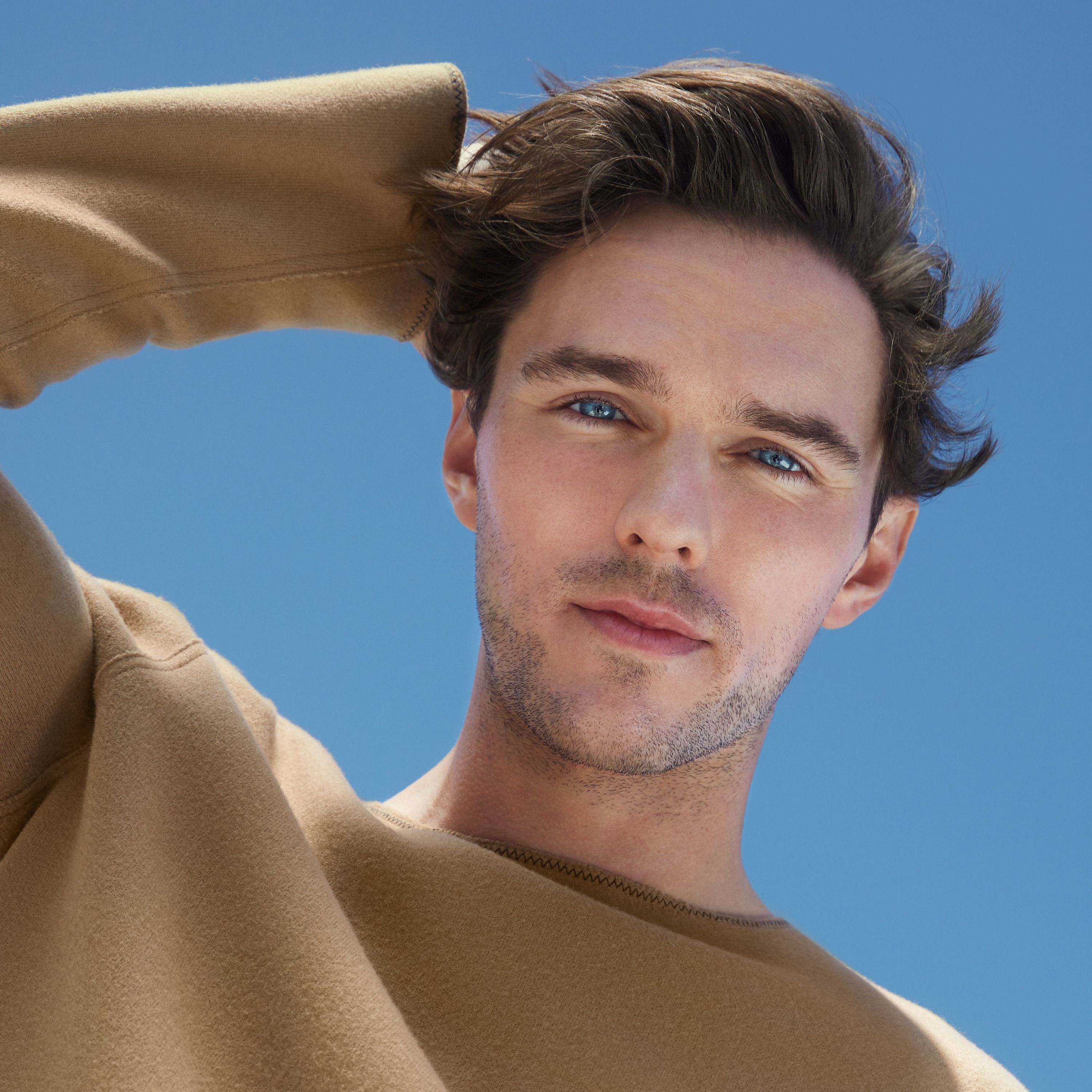 Porträt eines Mannes mit braunem Pullover und blauem Himmel.