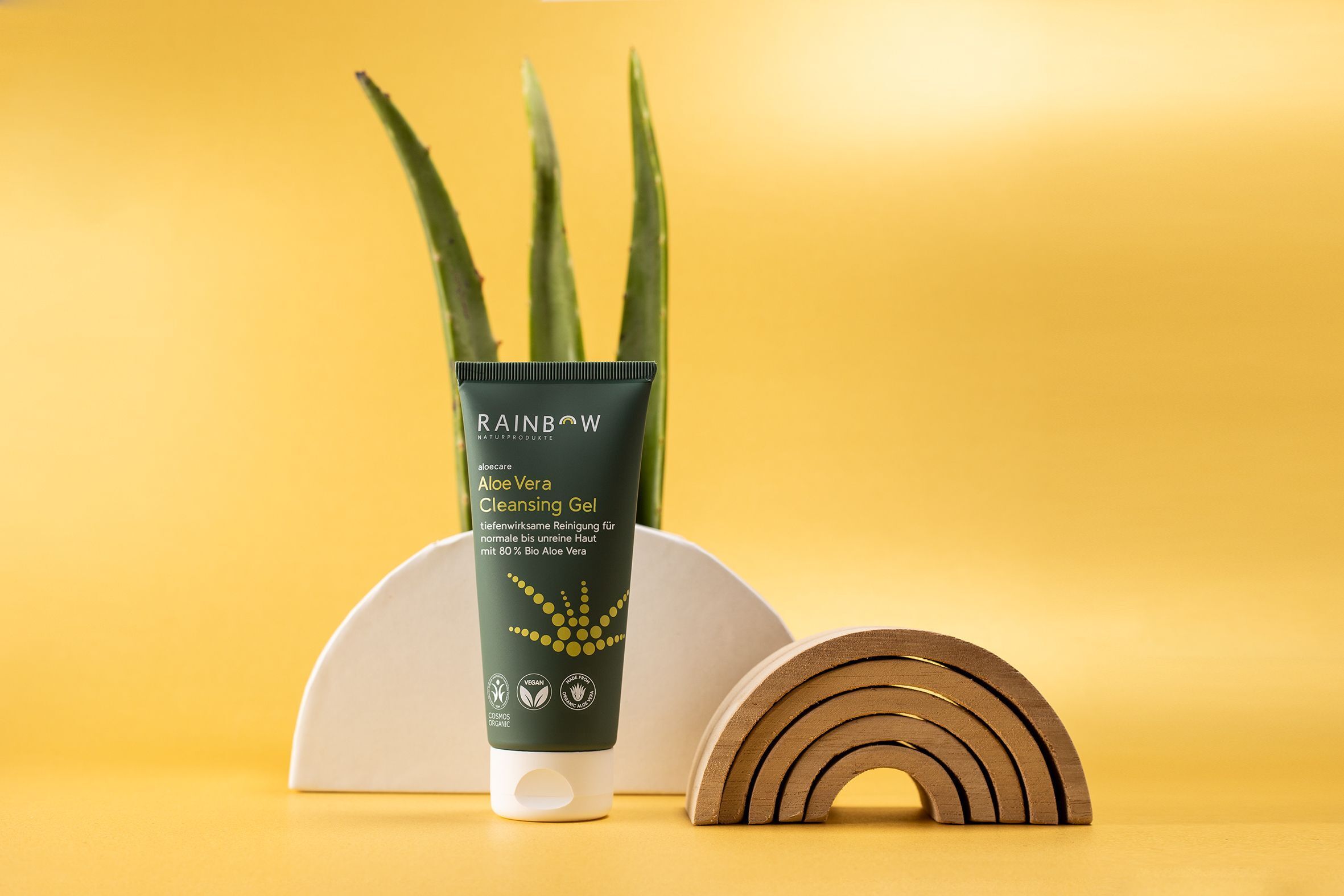 Eine Tube Rainbow aloecare Aloe Vera Cleansing Gel mit Aloe-Vera-Blättern und Holzdeko.