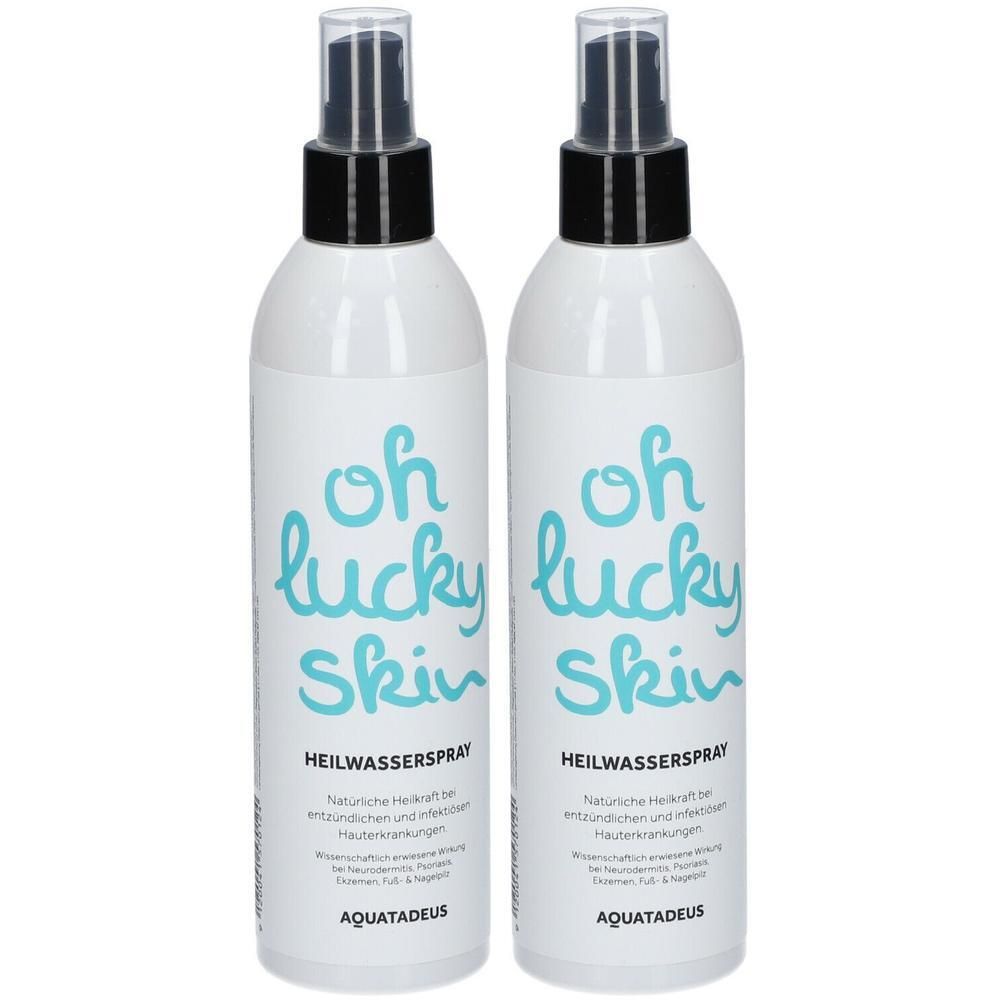 Zwei weiße Sprühflaschen mit schwarzem Sprühkopf. Blaue Schrift: "oh lucky skin HEILWASSERS PRAY".