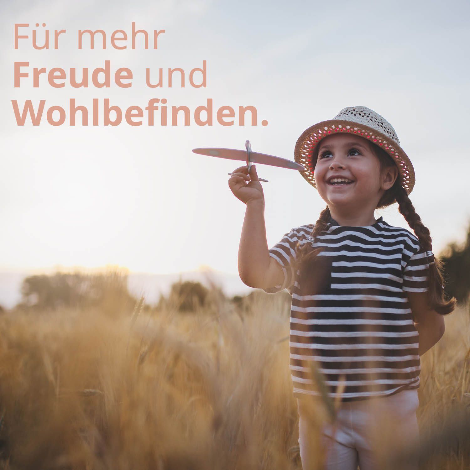 Ein Mädchen mit einem Spielzeugflugzeug in der Hand, trägt einen Strohhut und ein gestreiftes Shirt.