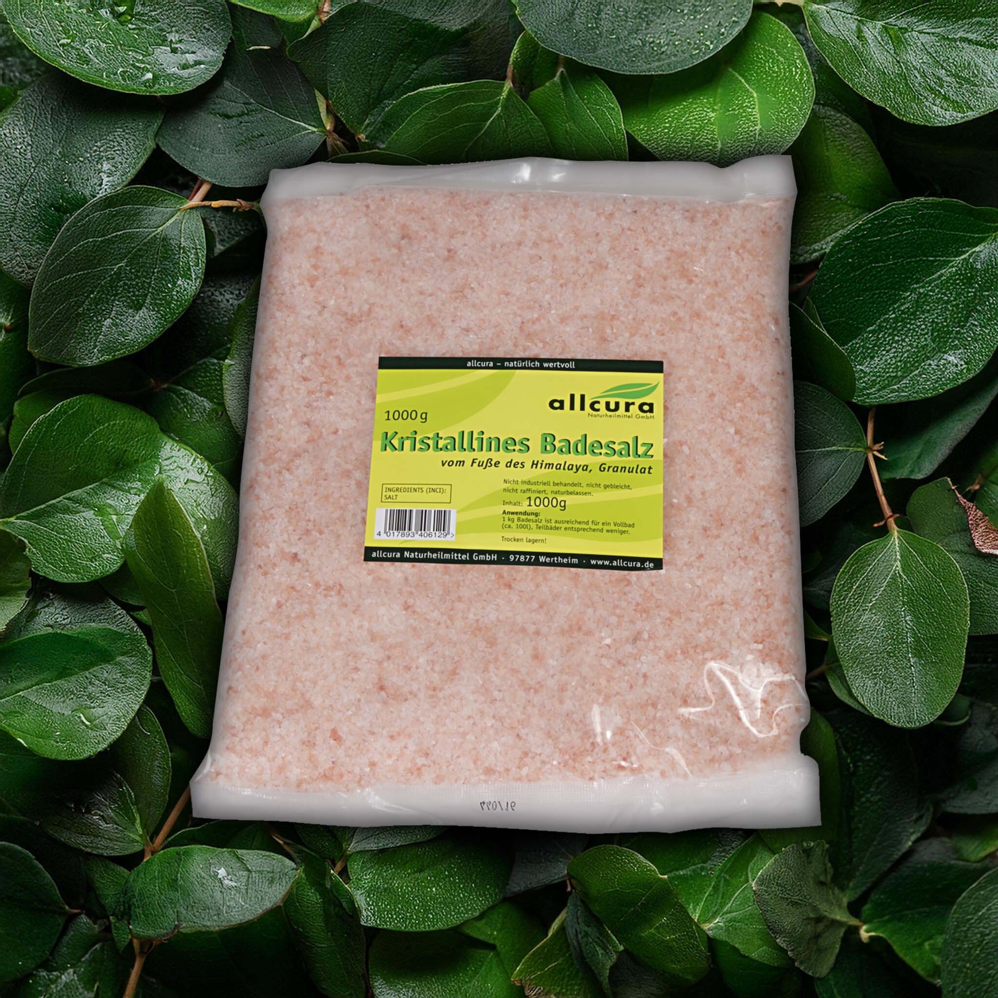 Produktverpackung mit rosafarbenem Badesalz, umgeben von grünen Blättern. Das Etikett zeigt Produktinformationen.