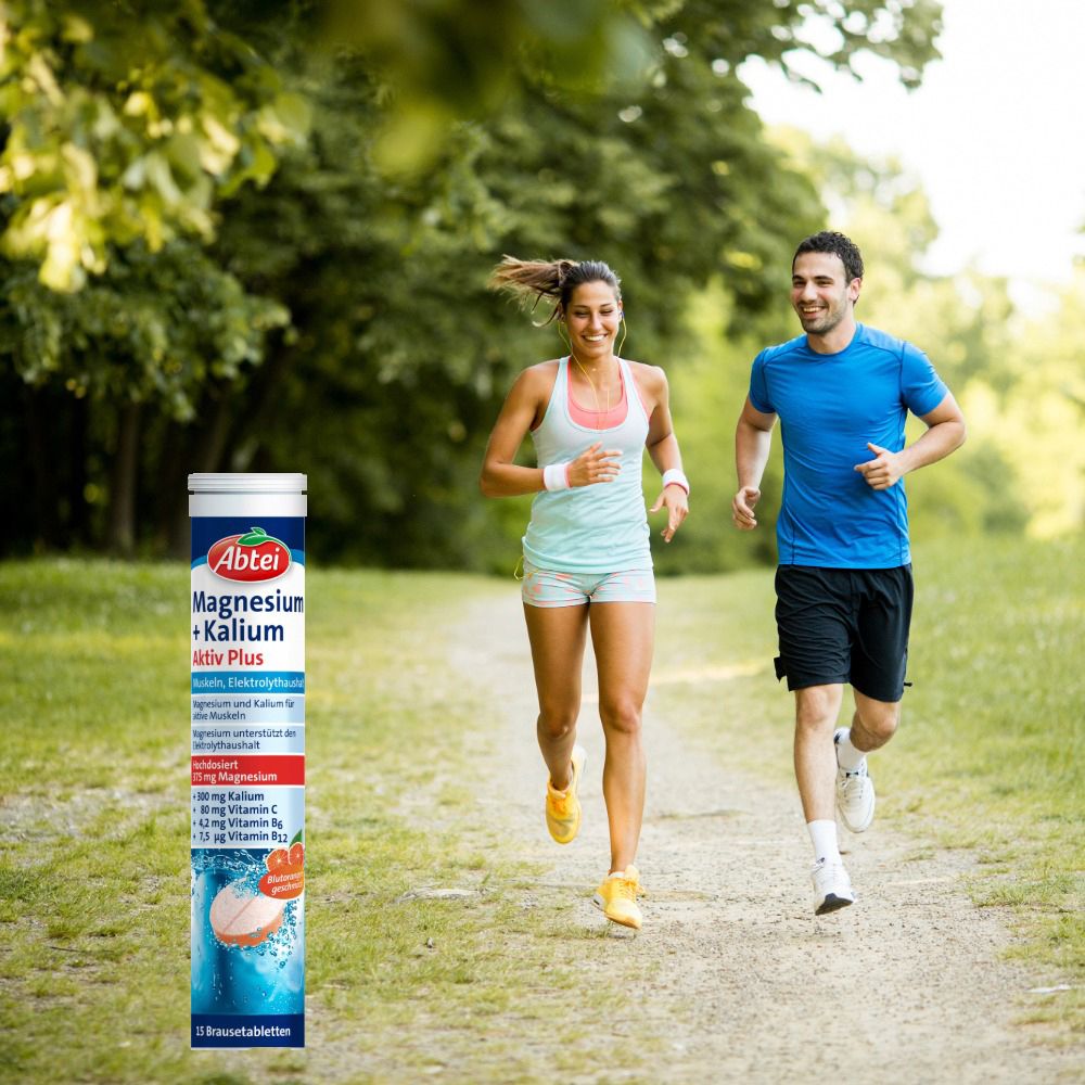 Zwei Personen joggen im Freien, eine hält eine Abtei Magnesium + Kalium Aktiv Plus Brausetabletten-Verpackung in der Hand.