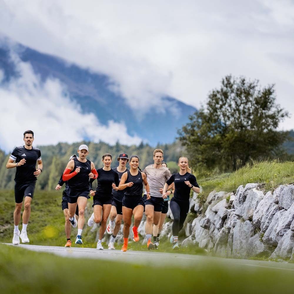 Gruppe von Läufern auf einer Straße. Berge und Bäume im Hintergrund. Sportbekleidung. Fokus auf Bewegung und Ausdauer.