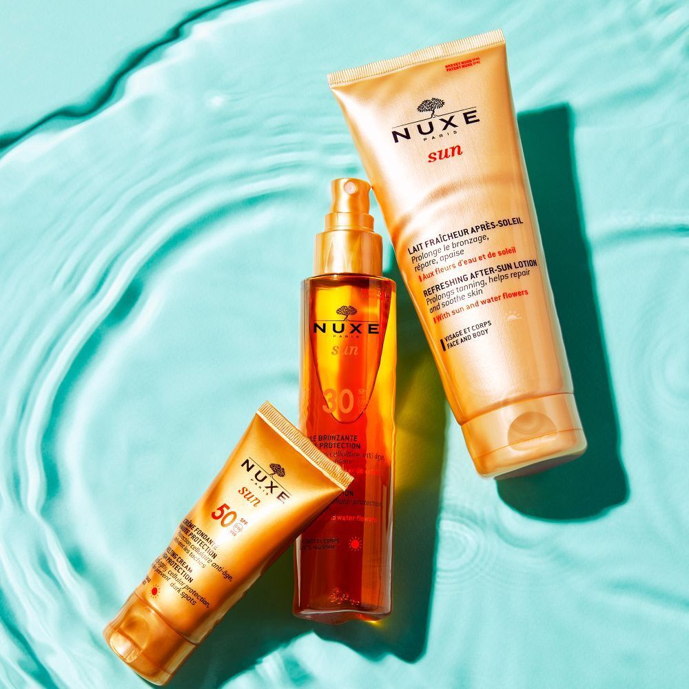 NUXE Sun Produkte in Wasser. Sonnenmilch, Öl und Spray. Gold- und Orangetöne. Text: Lait Fraîcheur Après-Soleil.