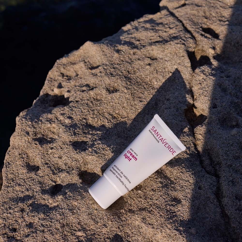 Weiße Tube "cream light" auf Stein. SANTAVERDE-Logo sichtbar. Produkt für Gesichtspflege. Schräge Perspektive.