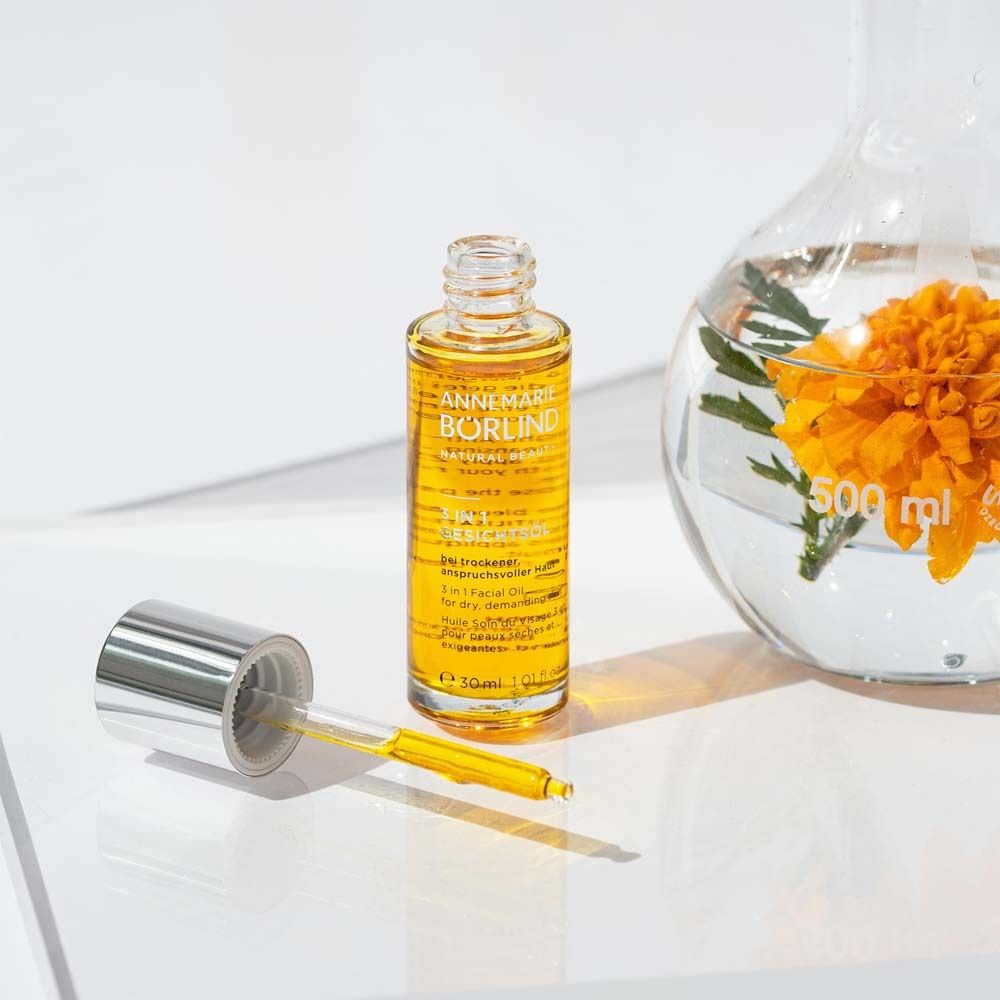 Gesichtsöl-Flasche mit Pipette neben einem Becherglas mit Blume. Produkt: ANNEMARIE BÖRLIND, 3 in 1 Gesichtsöl.