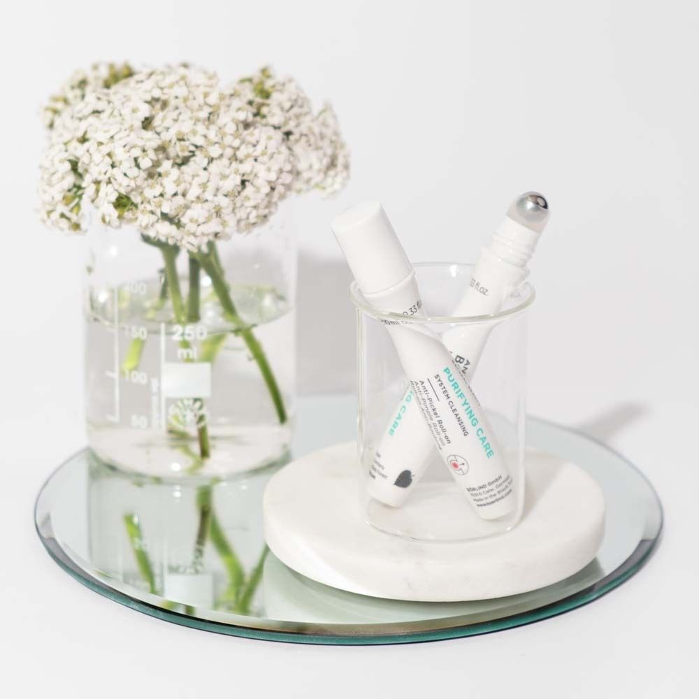 Zwei Roll-ons in Gläsern. Text: PURIFYING CARE. Marke: ANNEMARIE BÖRLIND. Auf Spiegel und Untersetzer.