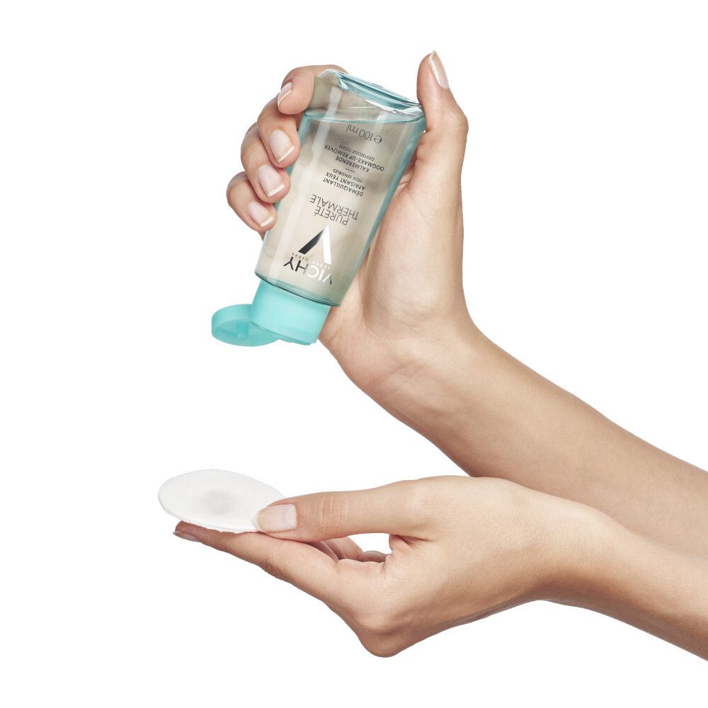 Hände halten eine Flasche und ein Wattepad. Flasche wird über das Pad gehalten, Flüssigkeit tropft heraus.
