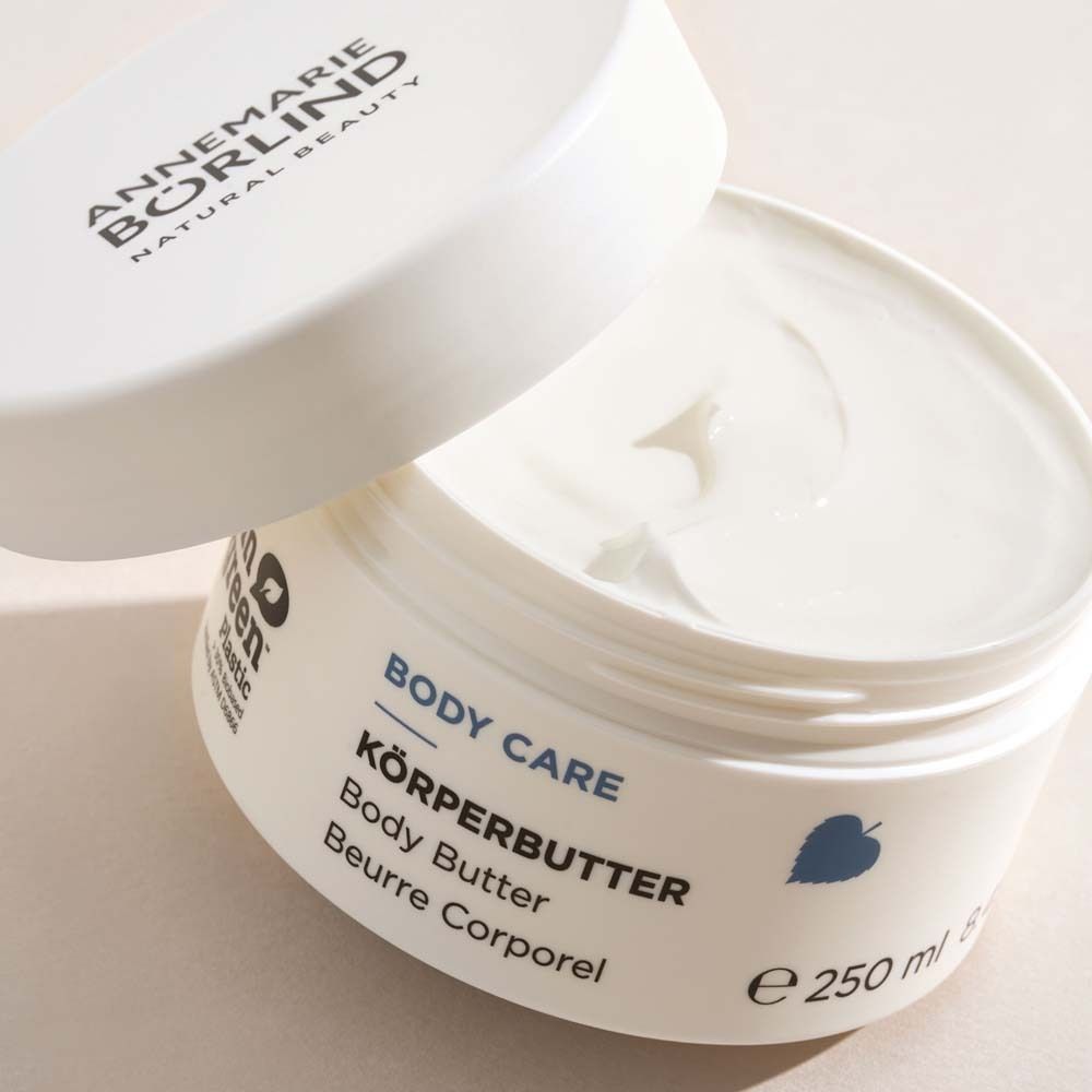 Weißer Tiegel mit geöffnetem Deckel. Aufschrift BODY CARE KÖRPERBUTTER. 250 ml.