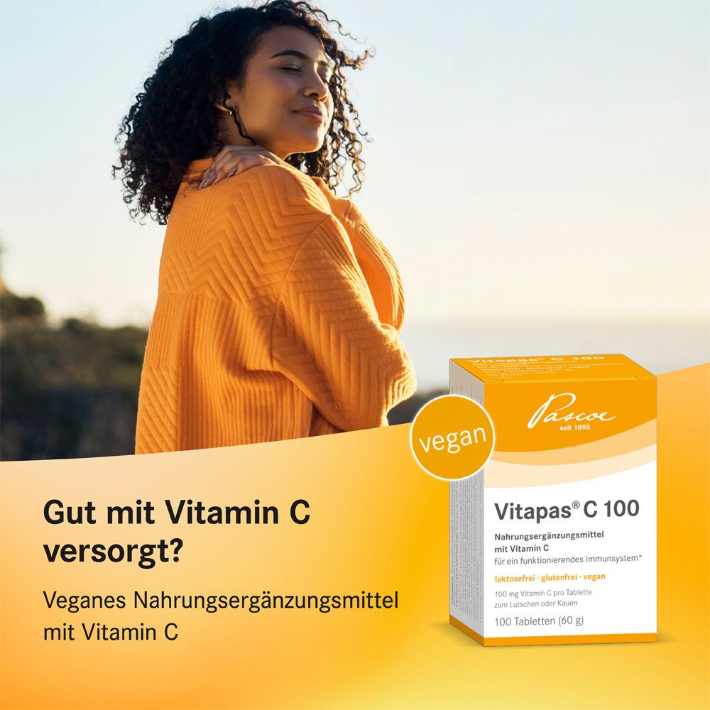 Frau mit Vitapas® C 100-Verpackung. Vegan-Label. Nahrungsergänzungsmittel mit Vitamin C. Orangefarbener Hintergrund.