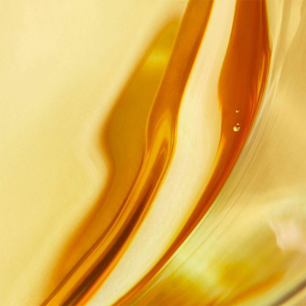 Abstrakte Nahaufnahme von goldfarbenen Flüssigkeiten mit Reflexionen. Zwei Tropfen sind sichtbar.