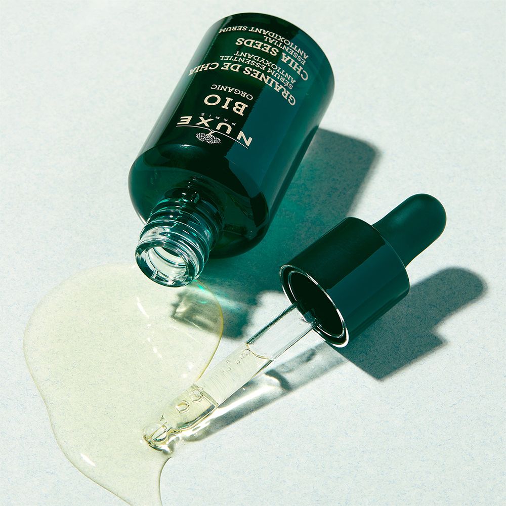 Grüne Glasflasche mit Pipette. Aufschrift: NUXE BIO, GRAINES DE CHIA, Serum essentiel antioxydant. Serum verschüttet.