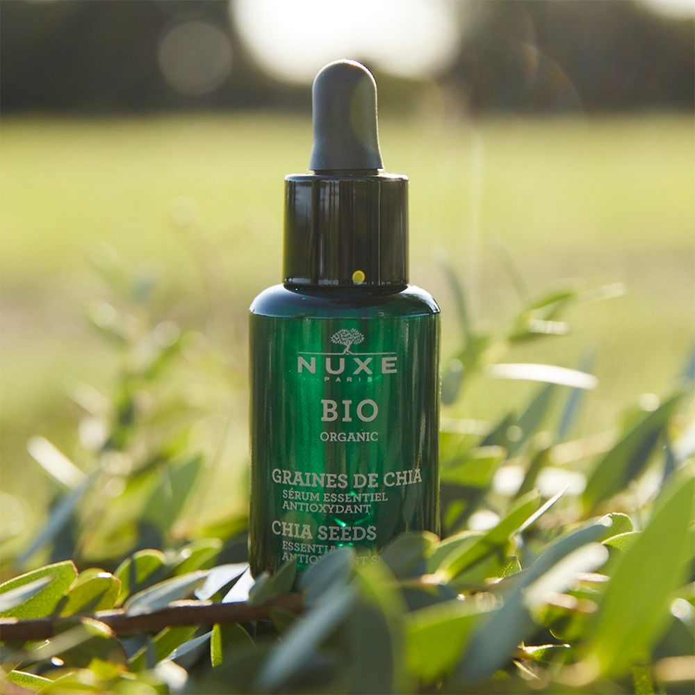 Grüne Glasflasche mit Pipette. Aufschrift: NUXE BIO, GRAINES DE CHIA, Serum essentiel antioxydant. Auf Blättern.