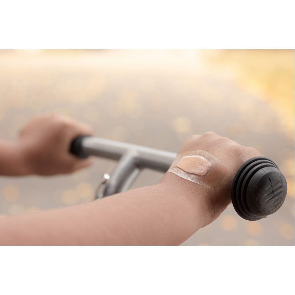 Kind mit Pflaster am Handgelenk. Pflaster ist transparent. Kind hält Lenker.