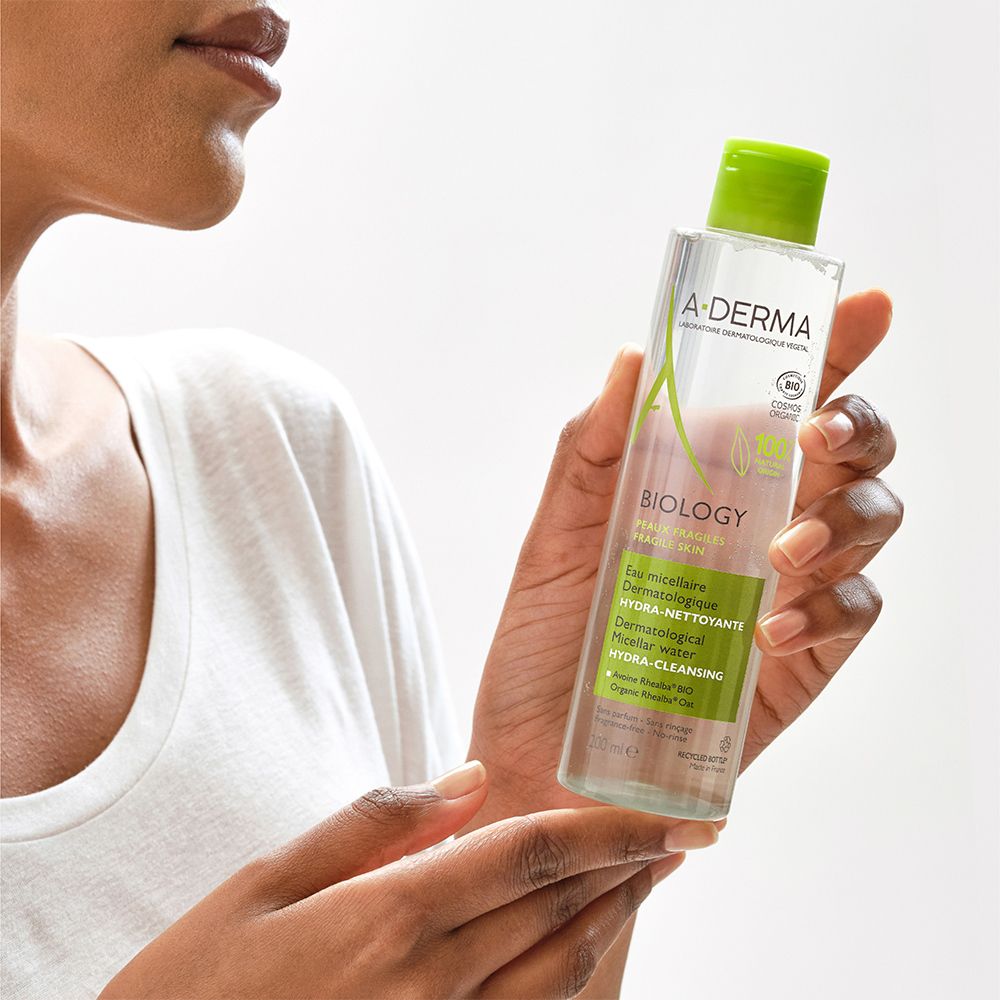 Person hält A-DERMA BIOLOGY Mizellenwasser. Flasche mit grünem Deckel und Etikett. Produkt für empfindliche Haut.