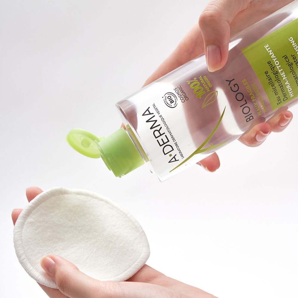 Hände halten A-DERMA BIOLOGY Mizellenwasser und Wattepad. Produkt wird auf Pad gegossen.