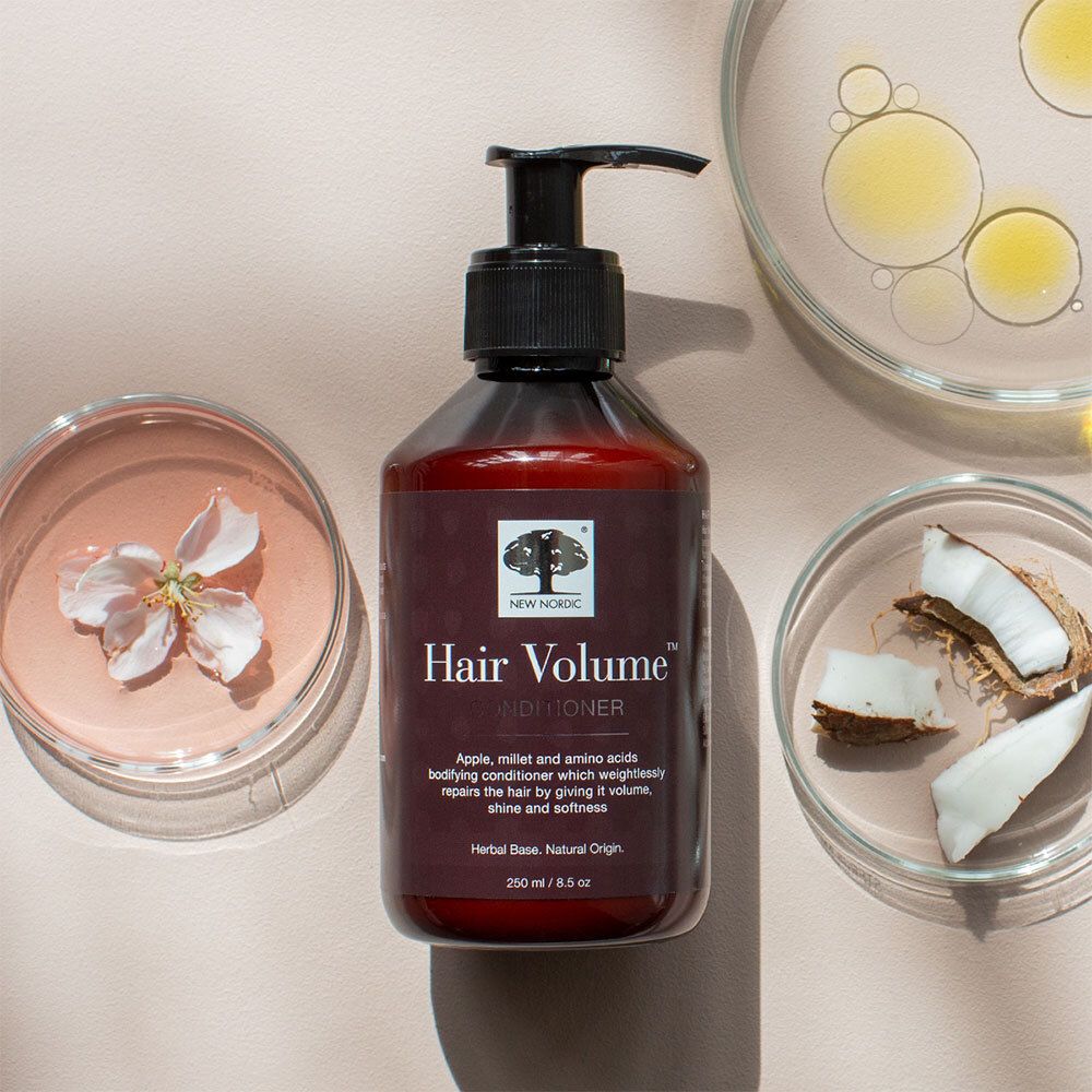 Braune Flasche mit schwarzem Pumpverschluss. Aufschrift: Hair Volume Conditioner. Umgeben von Blüten.