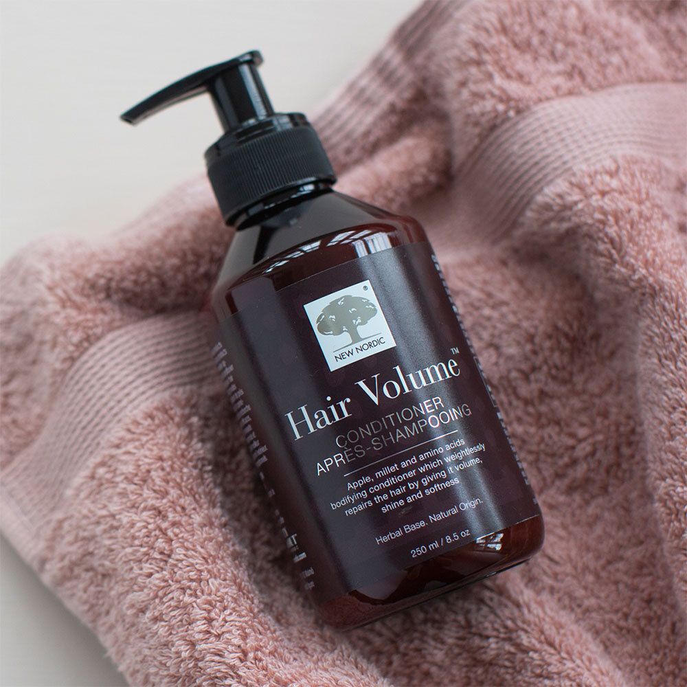 Braune Flasche mit schwarzem Pumpverschluss. Aufschrift: Hair Volume Conditioner. Auf rosa Handtuch.