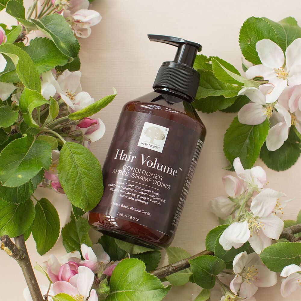 Braune Flasche mit schwarzem Pumpverschluss. Aufschrift: Hair Volume Conditioner. Umgeben von Blüten.