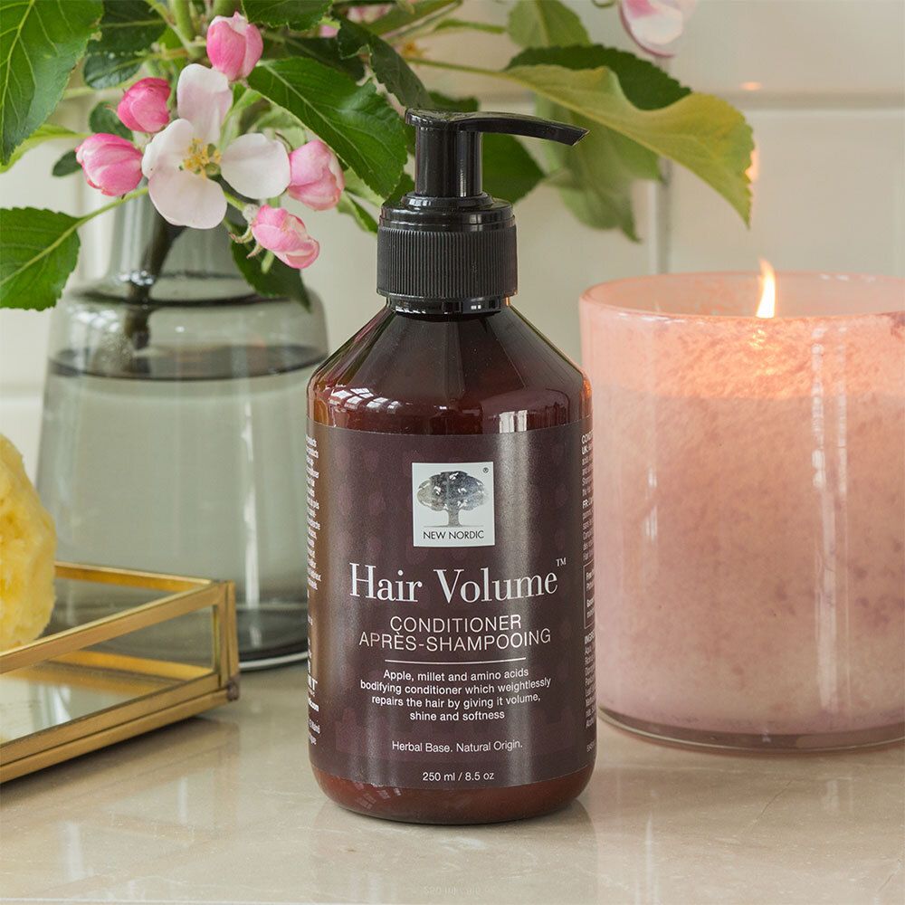 Braune Flasche mit schwarzem Pumpverschluss. Aufschrift: Hair Volume Conditioner. Neben Kerze und Vase.