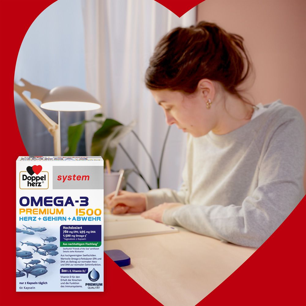 Produktverpackung von Doppelherz Omega-3 Premium 1500 auf einem Tisch. Eine Frau schreibt. Herzförmiger Hintergrund.
