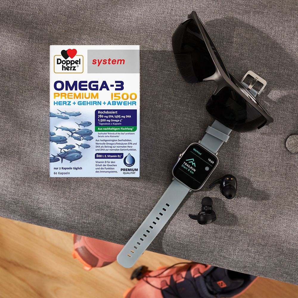 Produktverpackung von Doppelherz Omega-3 Premium 1500 neben Sonnenbrille, Smartwatch und Kopfhörern auf einem Tisch.