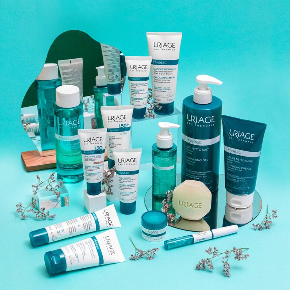 Produktpräsentation von Uriage Hyséac. Verschiedene Produkte auf blauem Grund. Flaschen, Tuben, Tiegel, und eine Seife.