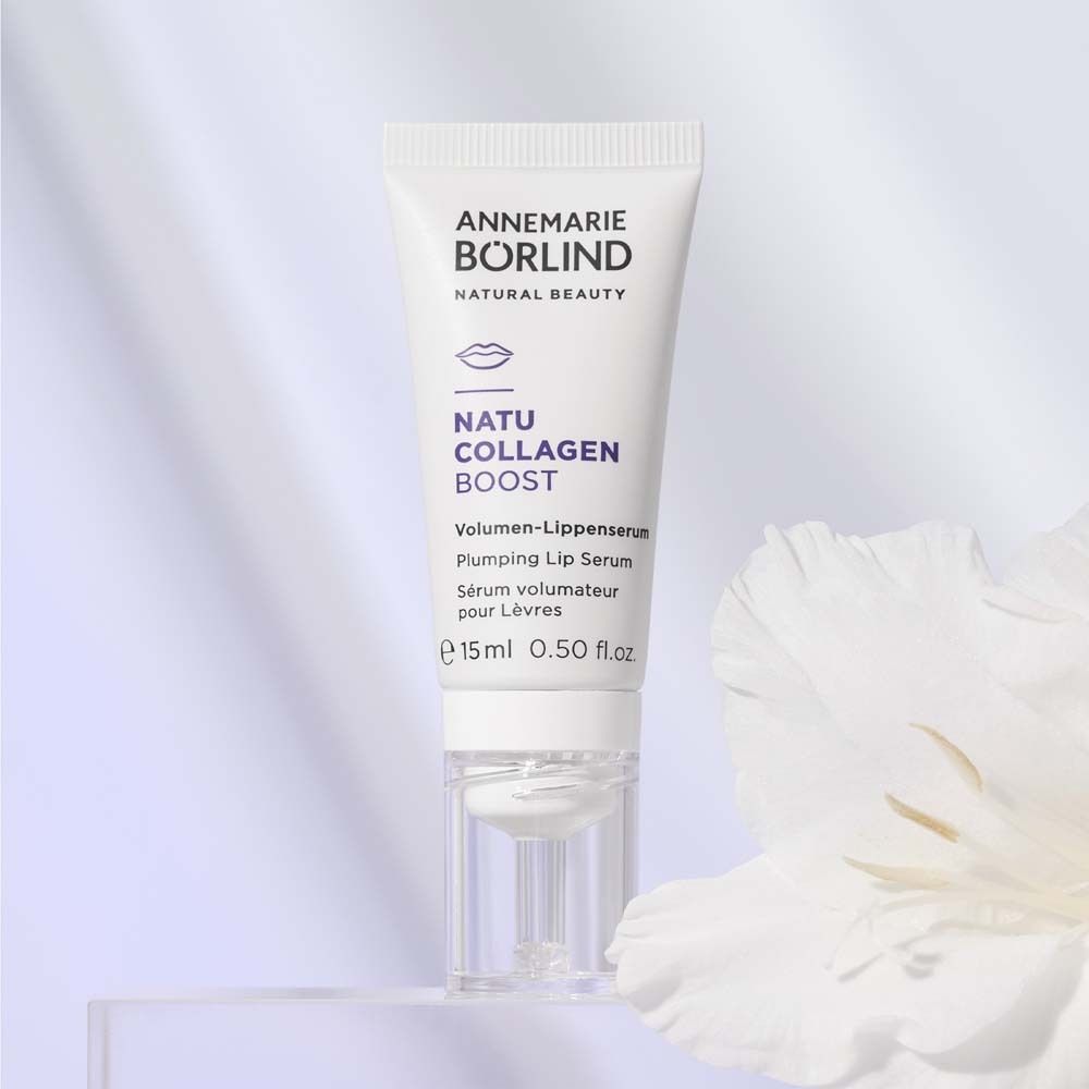 Weißes Lippen-Serum mit Schriftzug. Marke: ANNEMARIE BÖRLIND. Produktname: NATU COLLAGEN BOOST. Mit Blume im Hintergrund.