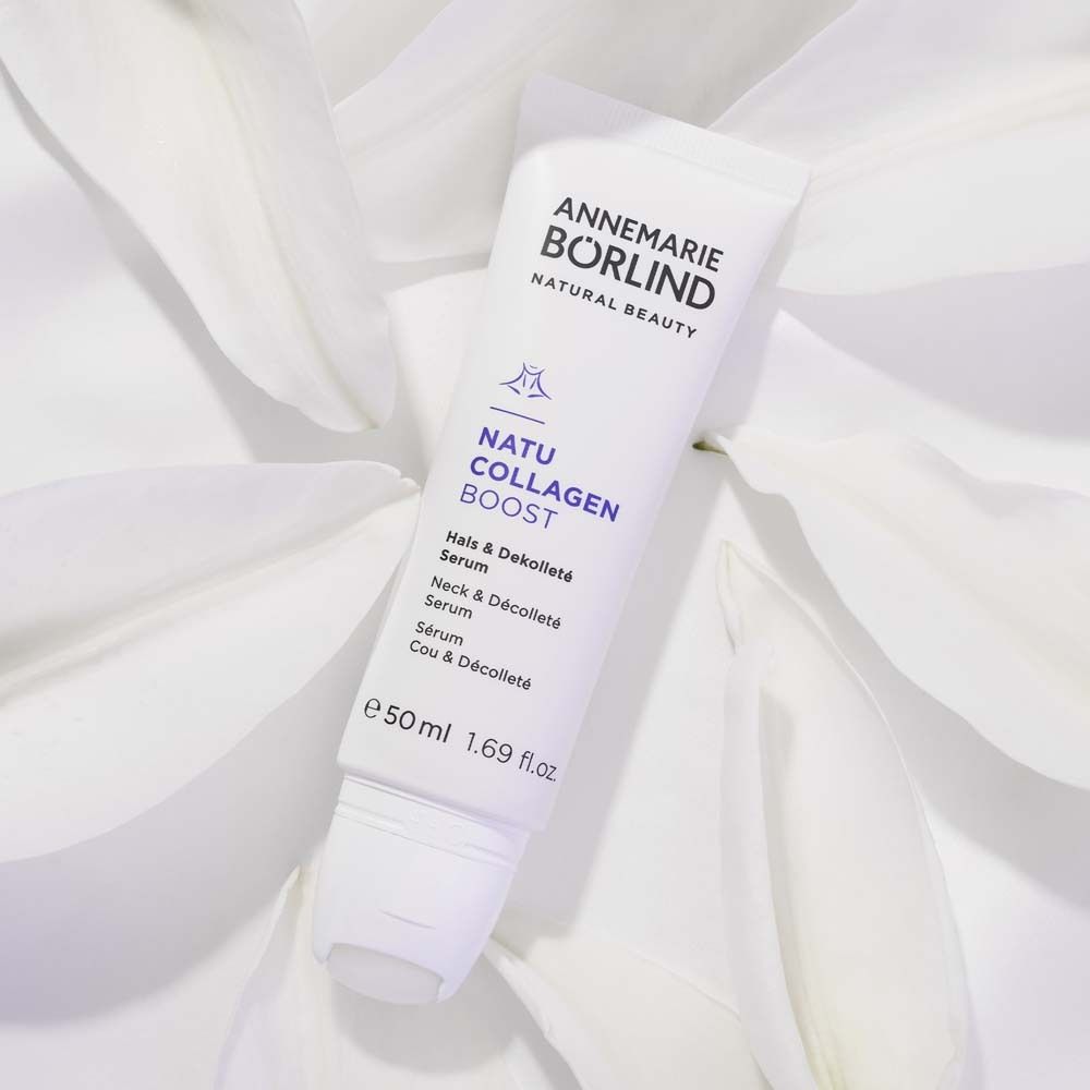 Creme-Tube mit Produktnamen und Marke. Weiß, mit lila Schrift. Auf weißen Blütenblättern.