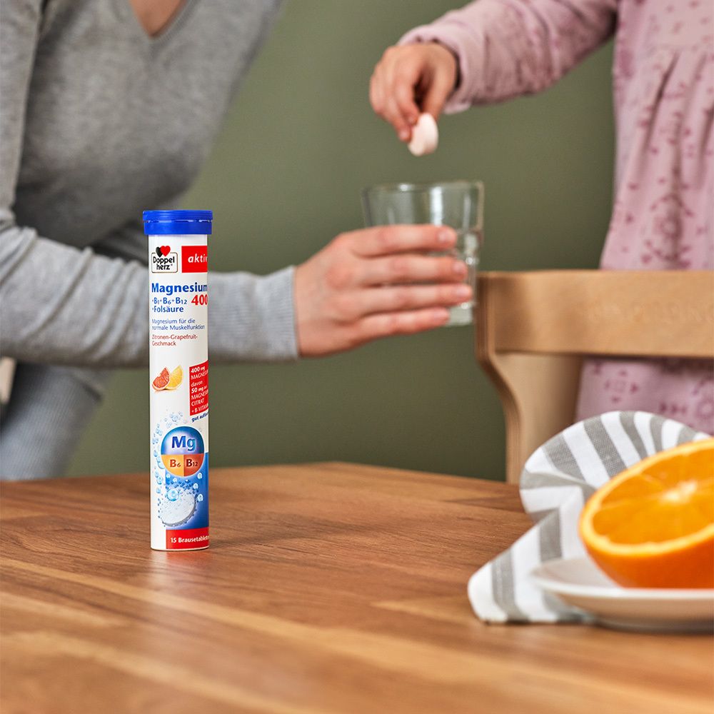 Personen halten eine Brausetablette und gießen Wasser in ein Glas. Daneben eine Packung Doppelherz Magnesium 400.
