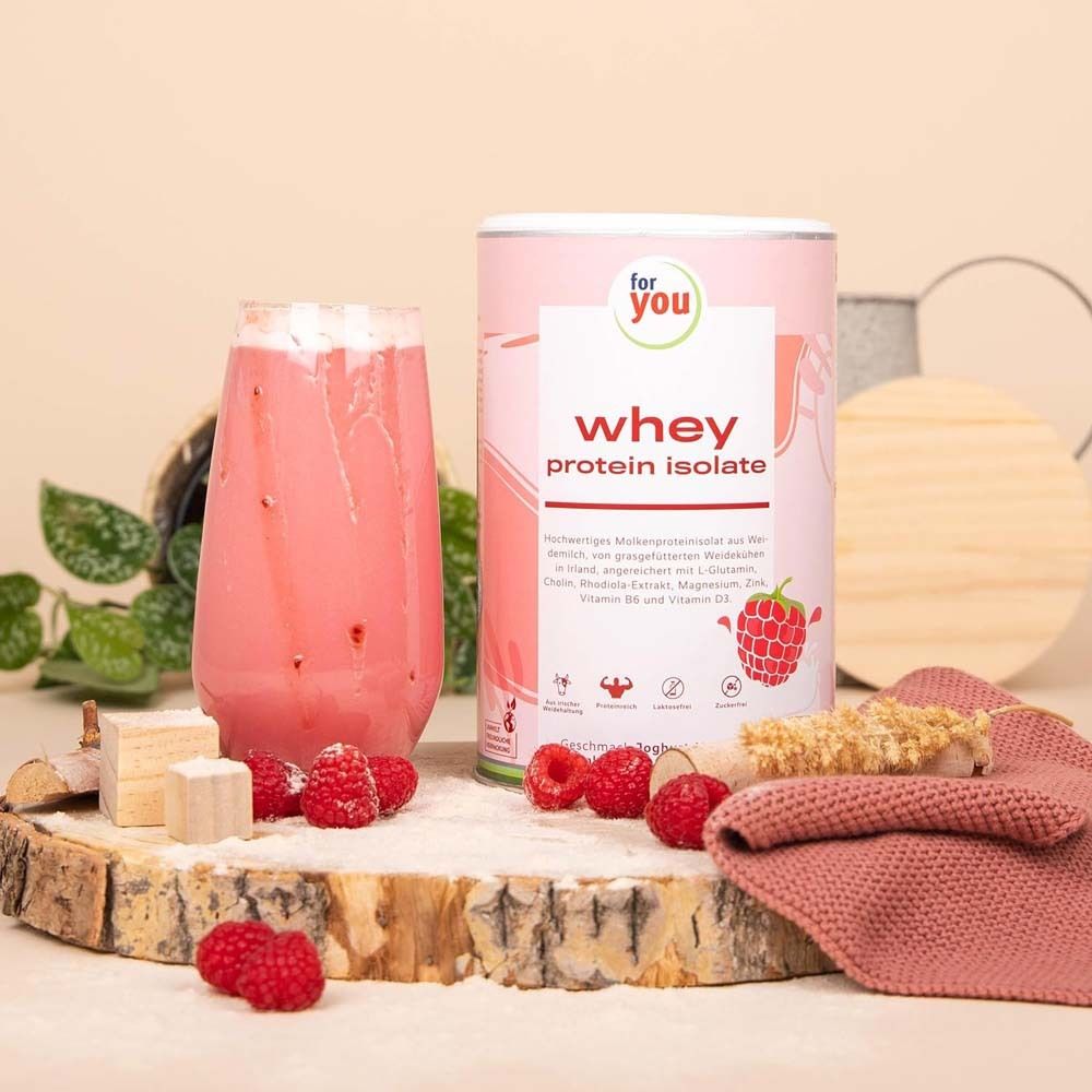 Glas mit rosa Shake, Himbeeren und Dose "whey protein isolate". Auf Holzbrett mit Zutaten. Hintergrund unscharf.
