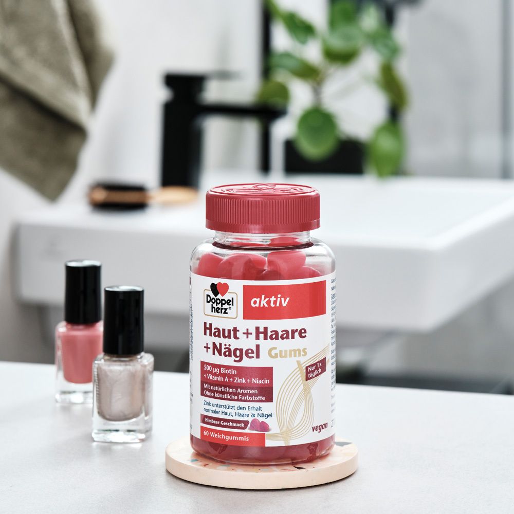 Doppelherz aktiv Haut + Haare + Nägel Gums auf Untersetzer. Daneben Nagellack. Rote Gummibärchen. Vegan.