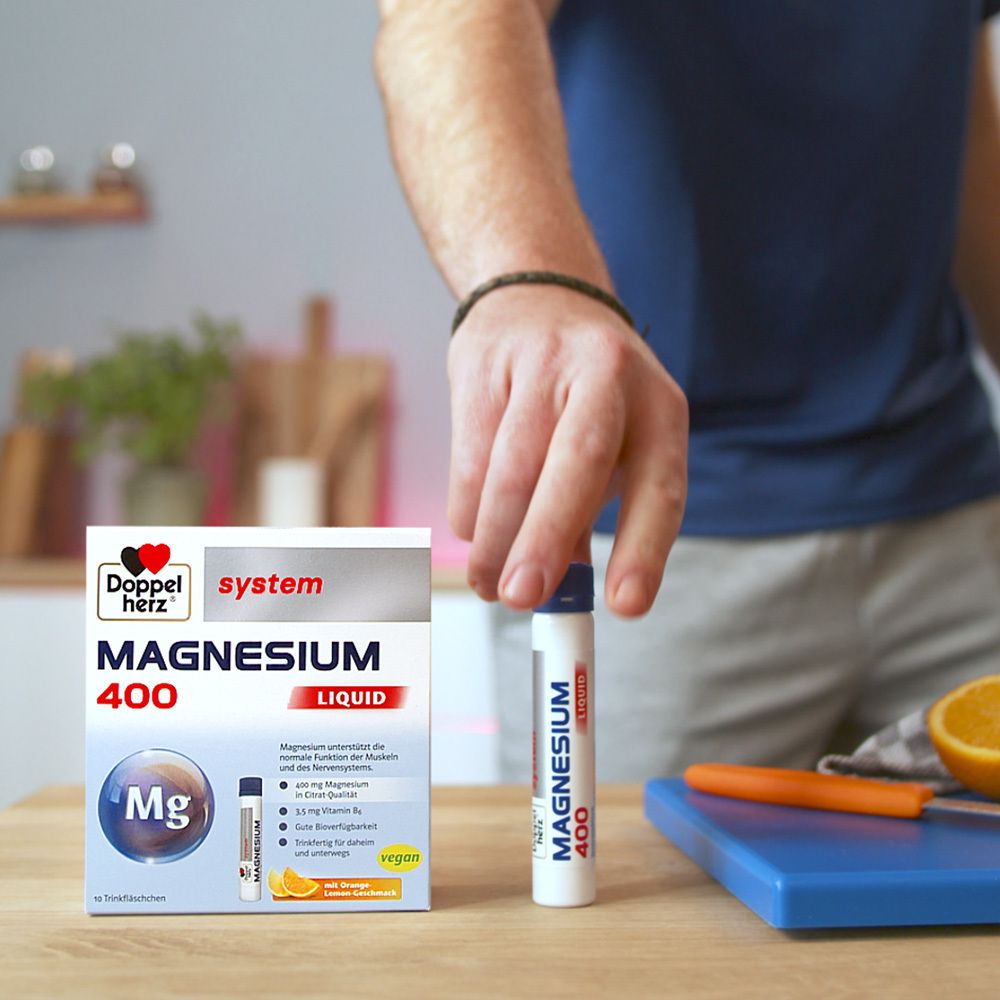 Person hält eine Trinkflasche "Magnesium 400 Liquid". Daneben Schachtel und Orange auf einem Schneidebrett.