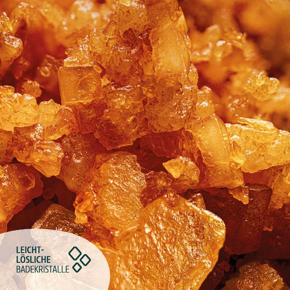 Nahaufnahme von orangefarbenen Badekristallen. Text: leicht lösliche Badekristalle.