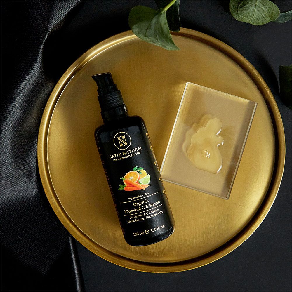Schwarze Flasche auf goldener Platte mit Serum. Aufschrift: SATIN NATUREL, Organic Vitamin A C E Serum.