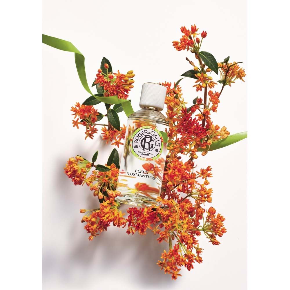 Glasflasche mit weißem Deckel, umgeben von orangefarbenen Blüten. Produktname: Fleur d'Osmanthus.