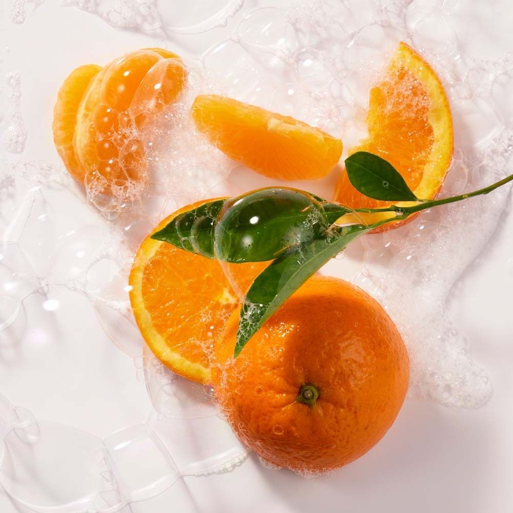 Orangenstücke und Blätter in Seifenblasen auf weißem Untergrund.