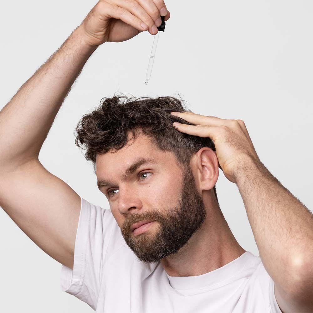 Mann hält Pipette über seinen Kopf. Serum wird aufgetragen.