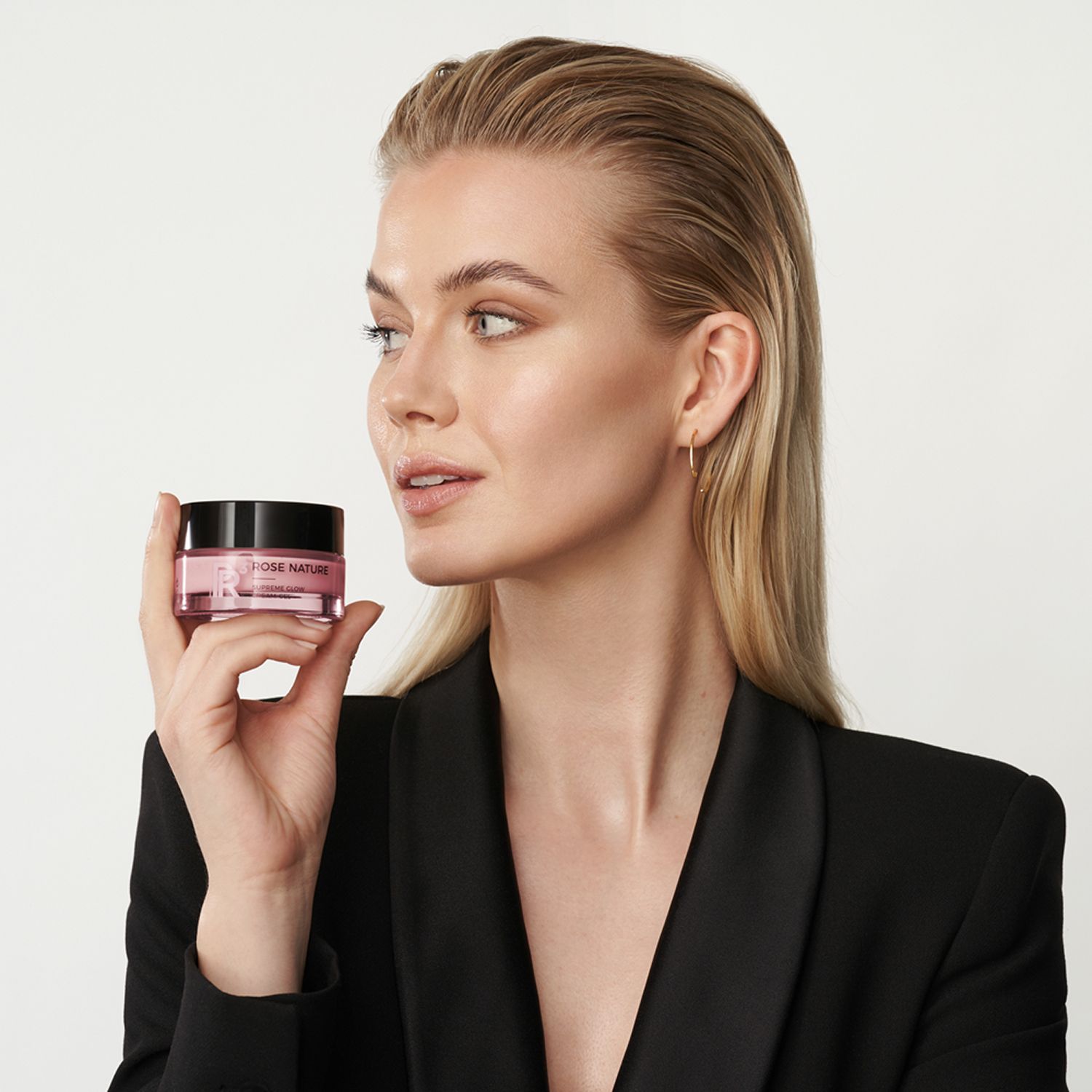 Frau hält eine kleine rosa Creme-Dose. Aufschrift: Rose Nature. Sie trägt einen schwarzen Blazer.