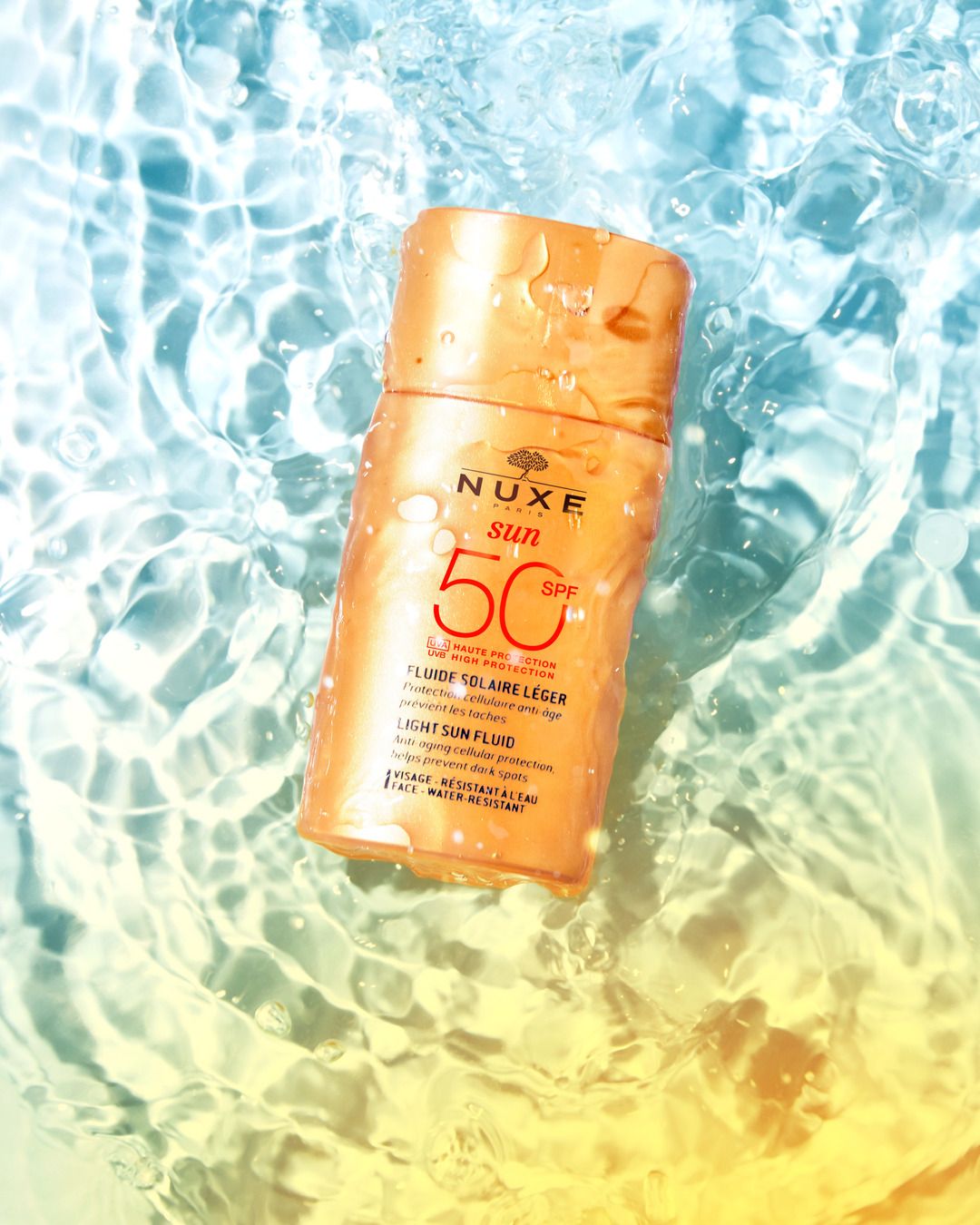 Sonnenfluid-Flasche im Wasser. Aufschrift: NUXE Sun, SPF 50. Text: Fluide solaire léger, Light Sun Fluid.