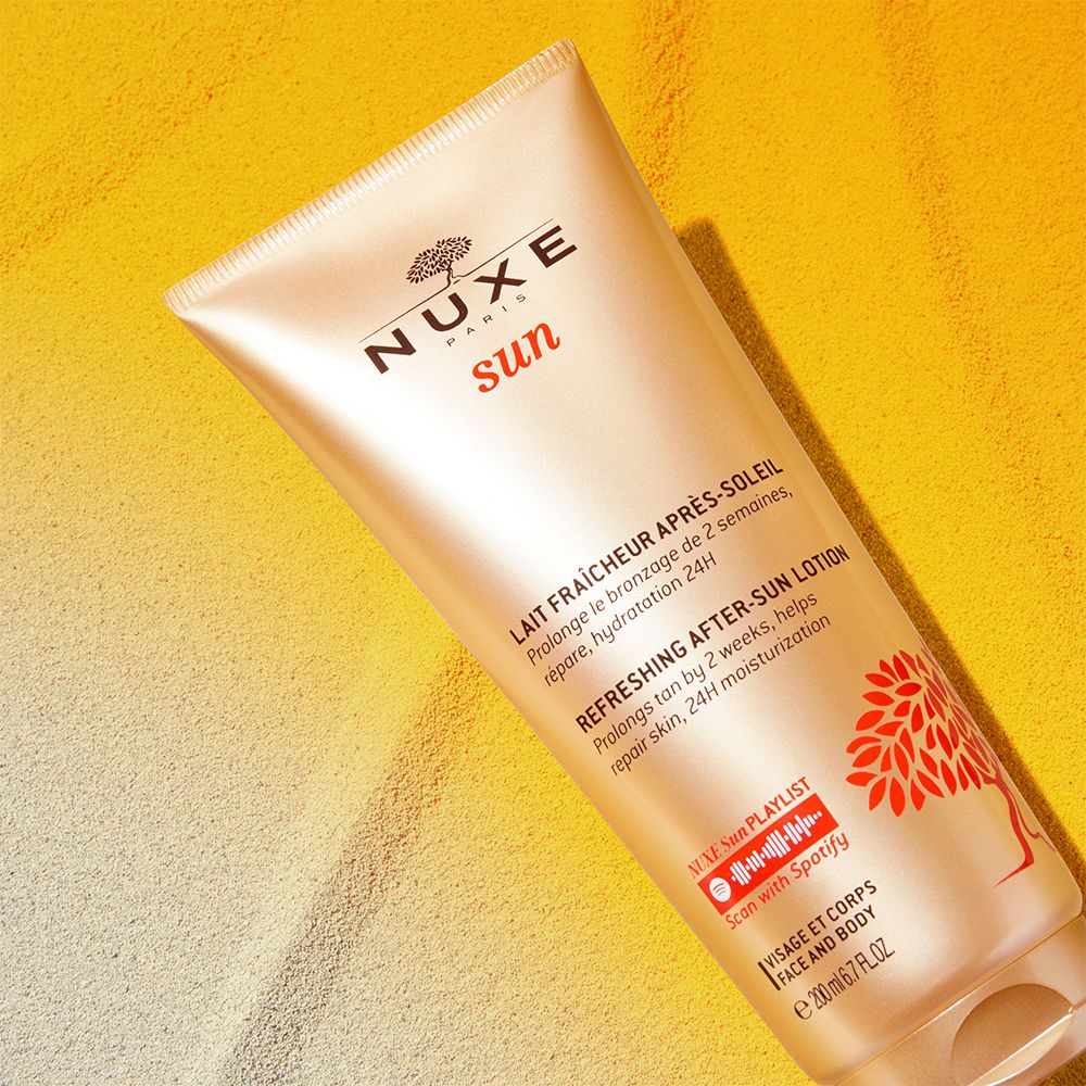 Tube NUXE Sun After-Sun-Lotion auf gelbem Sand. Produktinformationen und Logo sichtbar.
