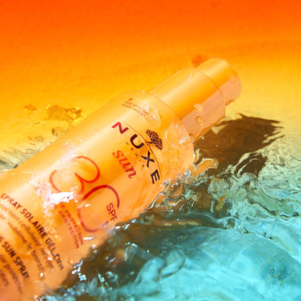 Gelbe Sprayflasche im Wasser. Aufschrift: NUXE Sun, SPF 30. Text: Spray Solaire Délicieux. Wasser spritzt.