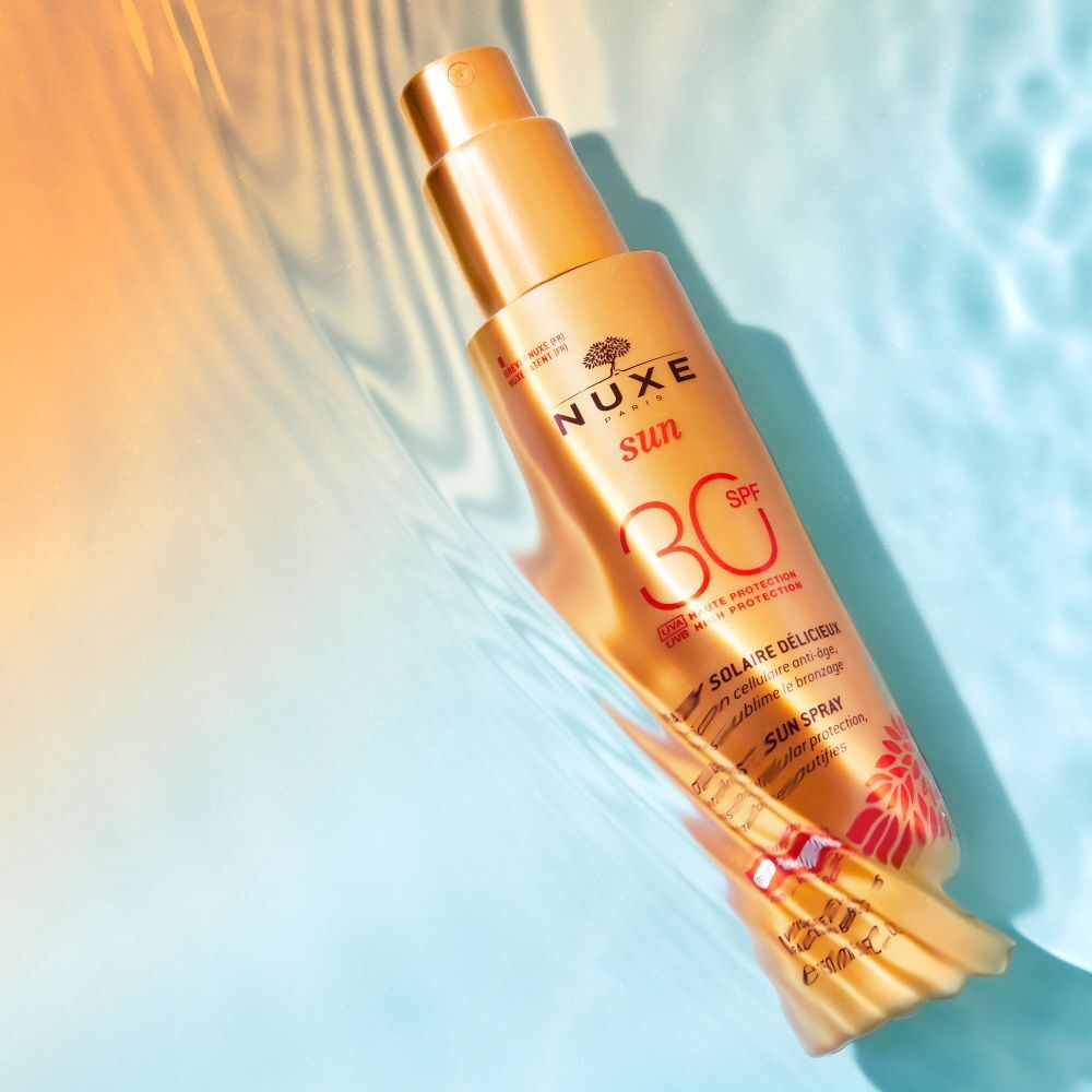 Gelbe Sprayflasche im Wasser. Aufschrift: NUXE Sun, SPF 30. Text: Spray Solaire Délicieux. Wasser spritzt.