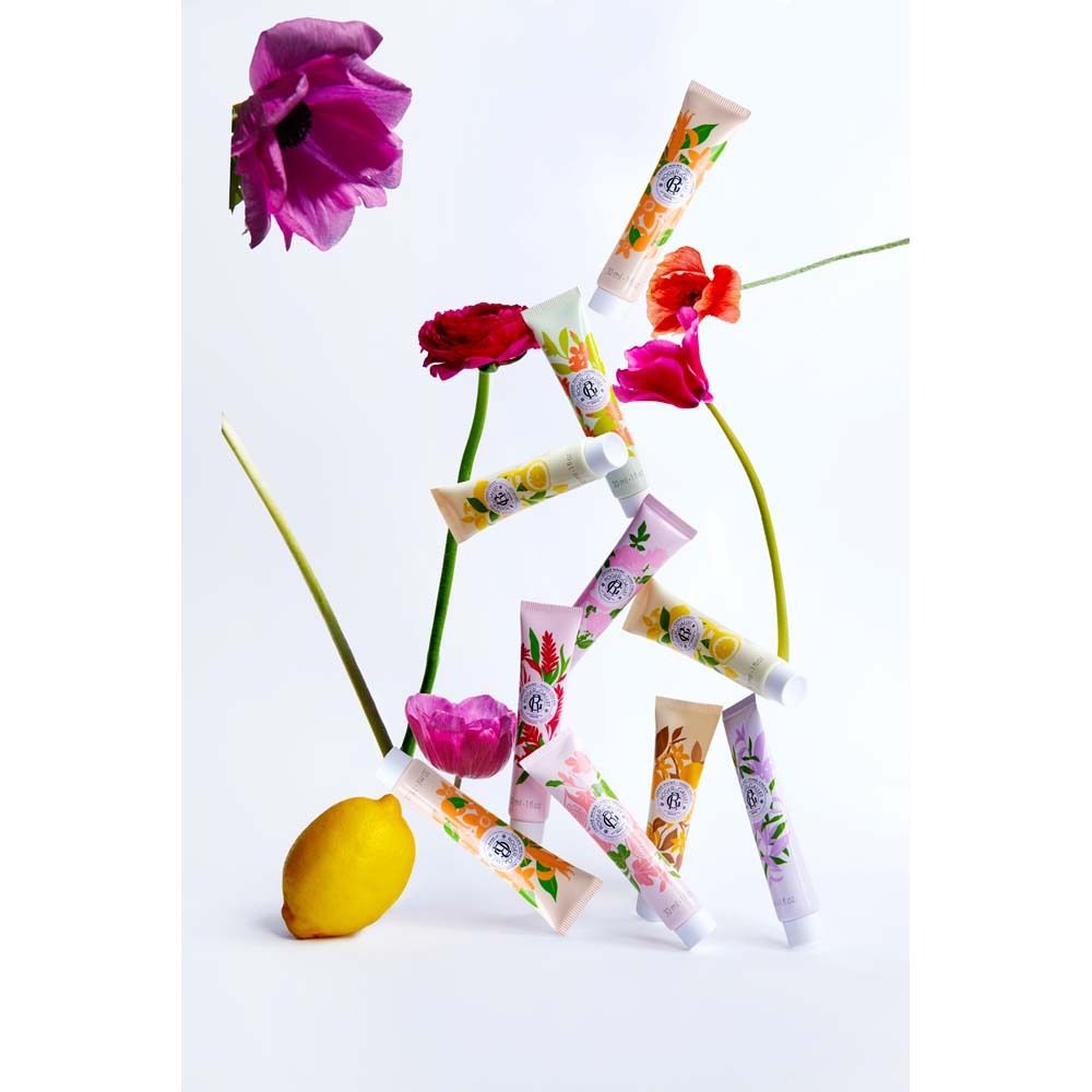 Mehrere Handcreme-Tuben mit floralem Design, umgeben von Blumen und einer Zitrone. Verschiedene Farben.