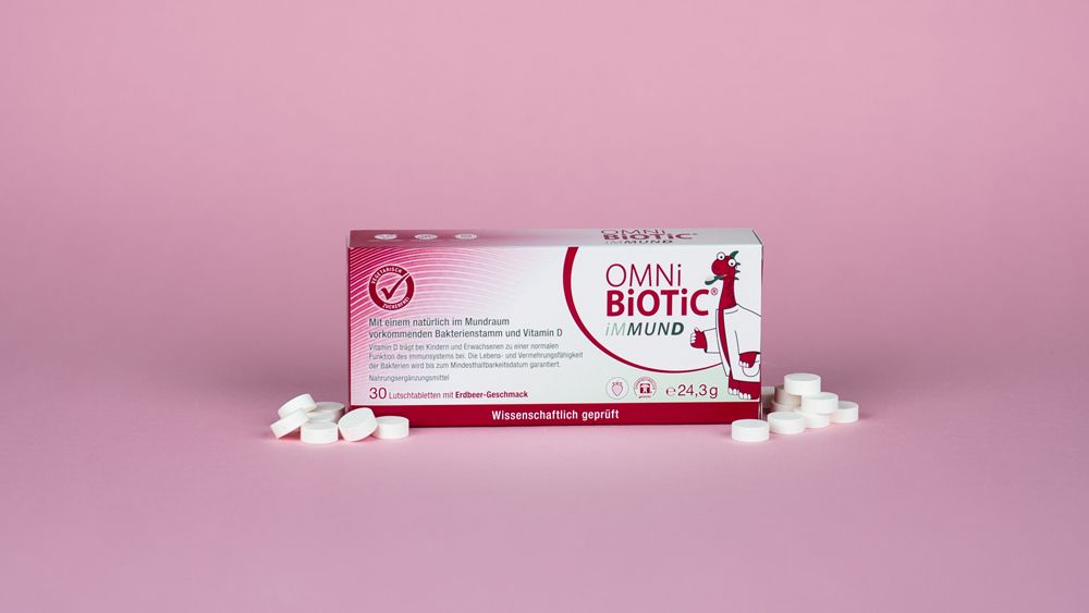 Packung OMNi-BiOTiC iMMUND und Lutschtabletten. Rosa Hintergrund. 30 Tabletten. Wissenschaftlich geprüft. Für Kinder und Erwachsene.