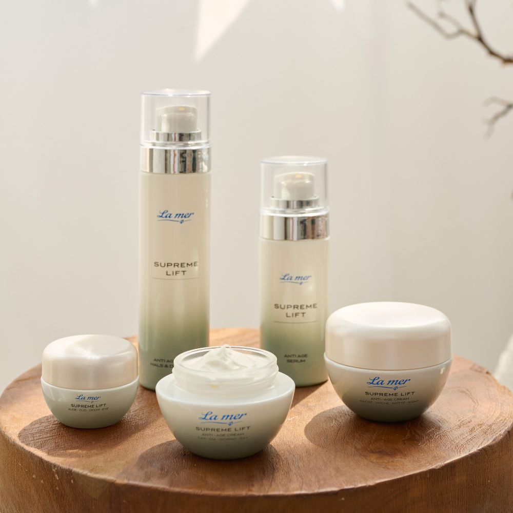 Verschiedene La mer SUPREME LIFT Produkte. Cremes, Seren, Flakons. Auf Holzoberfläche platziert.