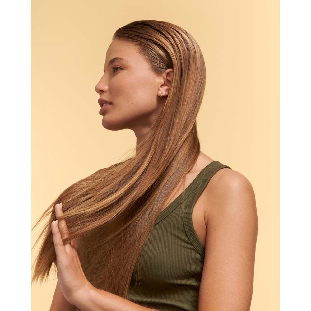 Frau mit langen, glänzenden Haaren. Sie berührt ihr Haar. Hintergrund gelb.