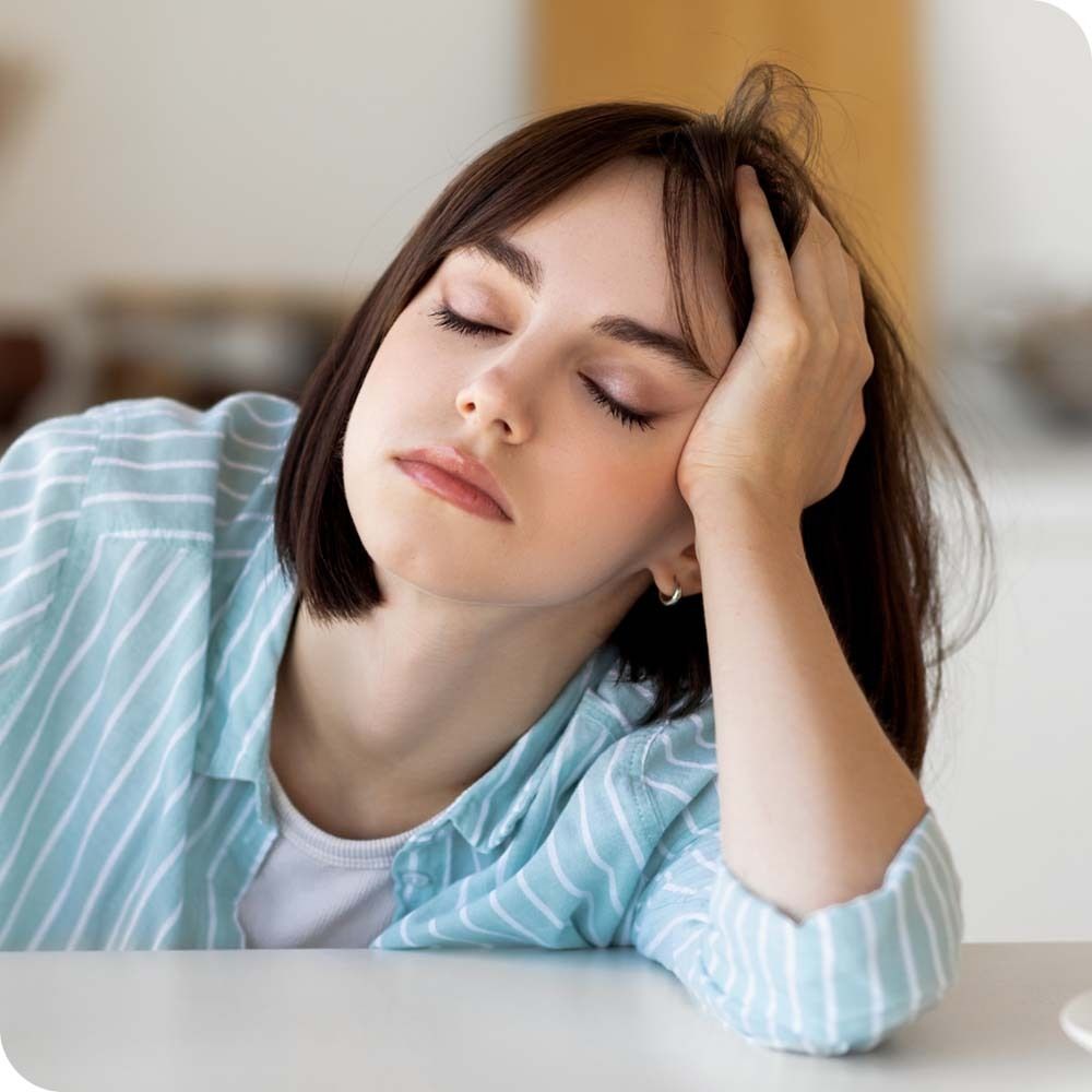 Eine junge Frau mit geschlossenen Augen, die ihren Kopf auf ihre Hand stützt. Sie trägt ein blaues Hemd.