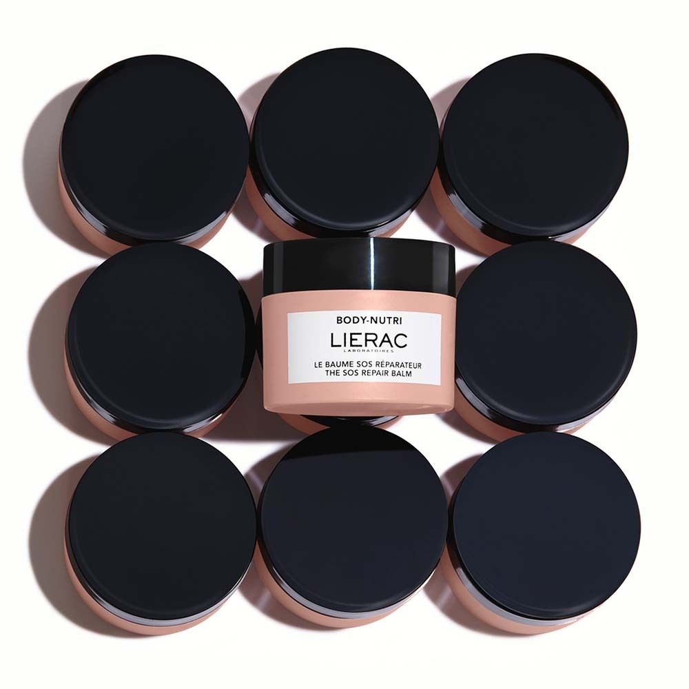 Acht Tiegel mit schwarzen Deckeln umgeben einen Tiegel mit weißem Etikett. Aufschrift: LIERAC, LE BAUME SOS RÉPARATEUR, THE SOS REPAIR BALM.